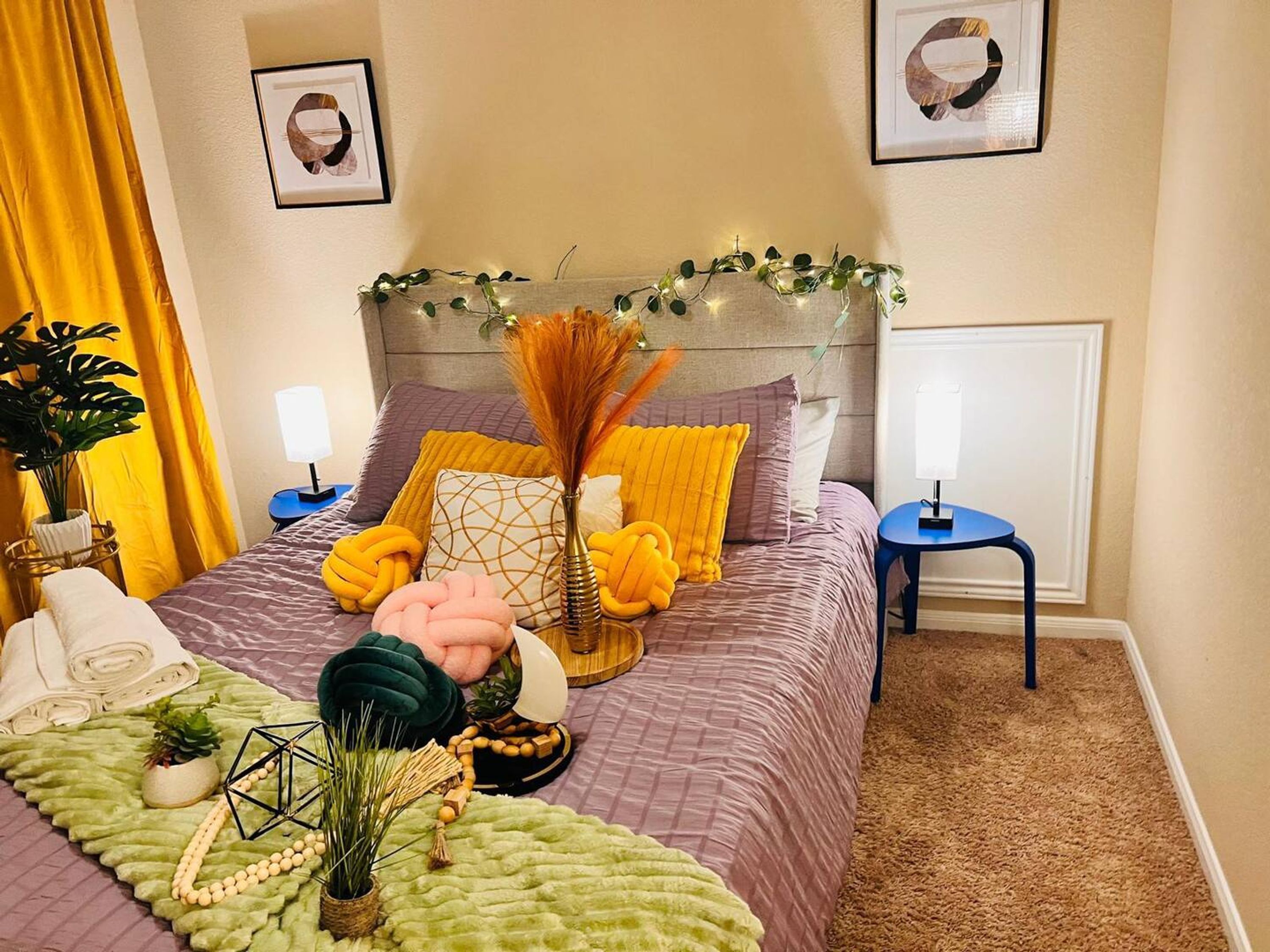 A neatly arranged bedroom with a bed, bedside tables, a small blue stool, and a decorative plant.