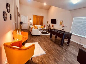 Un salon comprenant un canapé, une table basse, un baby-foot et un fauteuil orange vif.