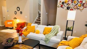 A modern living room with a white sofa, yellow throw pillows, a wooden coffee table, and a floor lamp. - Spacious 4BR Home w Game Room Office Backyard (Kyle)