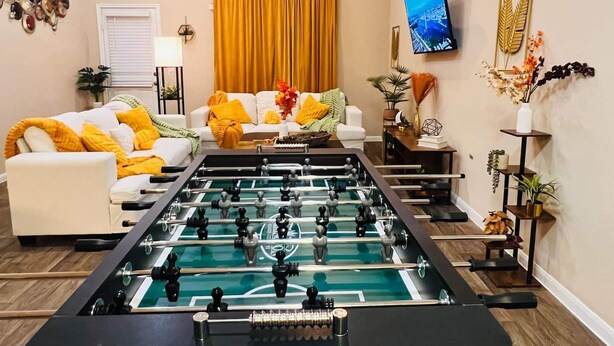A living room with a foosball table, a sofa, and a TV mounted on the wall. - Spacious 4BR Home w Game Room Office Backyard (Kyle)