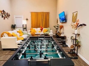A living room with a foosball table, a sofa, and a TV mounted on the wall. - Spacious 4BR Home w Game Room Office Backyard (Kyle)