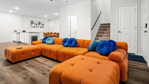 Una sala de estar moderna con un sofá modular, un ventilador de techo y una escalera que lleva a otro nivel.