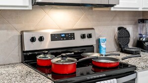 Una cocina con estufa de acero inoxidable, ollas rojas, un fabricante de gofres y una caja de cereales.