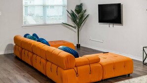 Una sala de estar con un sofá seccional naranja, una planta en maceta y un televisor montado.