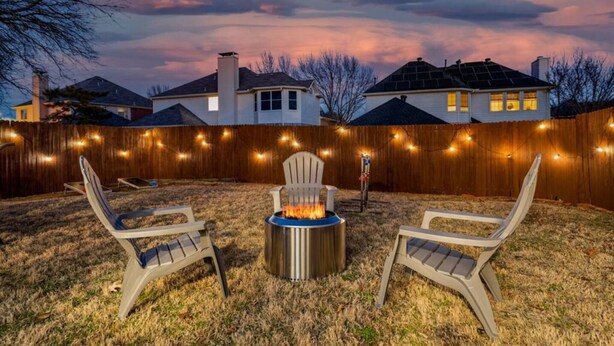 A backyard with a fire pit, two lawn chairs, and a wooden fence. - Stylish One Level Home Ping Pong Foosball Yard (Frisco)