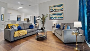 A modern living room with two grey sofas, a coffee table, and a lamp. There are abstract paintings on the wall and a blue curtain. - Stylish One Level Home Ping Pong Foosball Yard (Frisco)