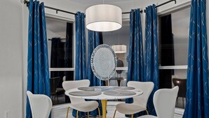 A dining area with a round table, white chairs, and a central mirror. Blue curtains with a pattern hang on the windows. - Stylish One Level Home Ping Pong Foosball Yard (Frisco)