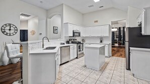 A modern kitchen with white cabinetry, a central island, and a built-in oven. - Stylish One Level Home Ping Pong Foosball Yard (Frisco)