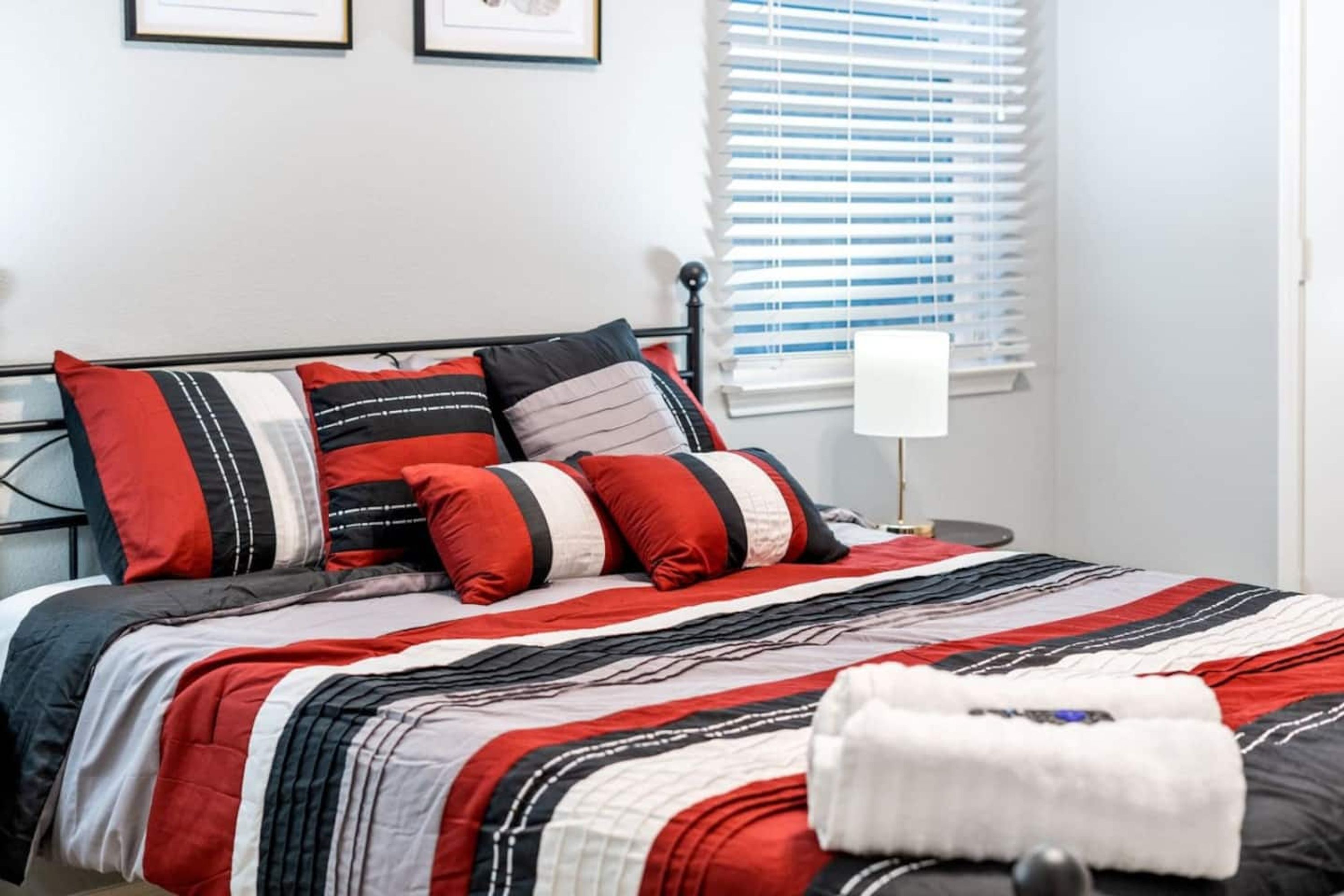 Un lit bien fait, avec une couvre-lit à rayures et plusieurs oreillers aux couleurs rouge, noir et blanc.