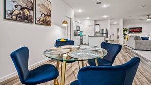 Un salon moderne avec une table à manger au plateau en verre entourée de chaises bleues, une cuisine en arrière-plan et un téléviseur affichant le logo de Netflix.