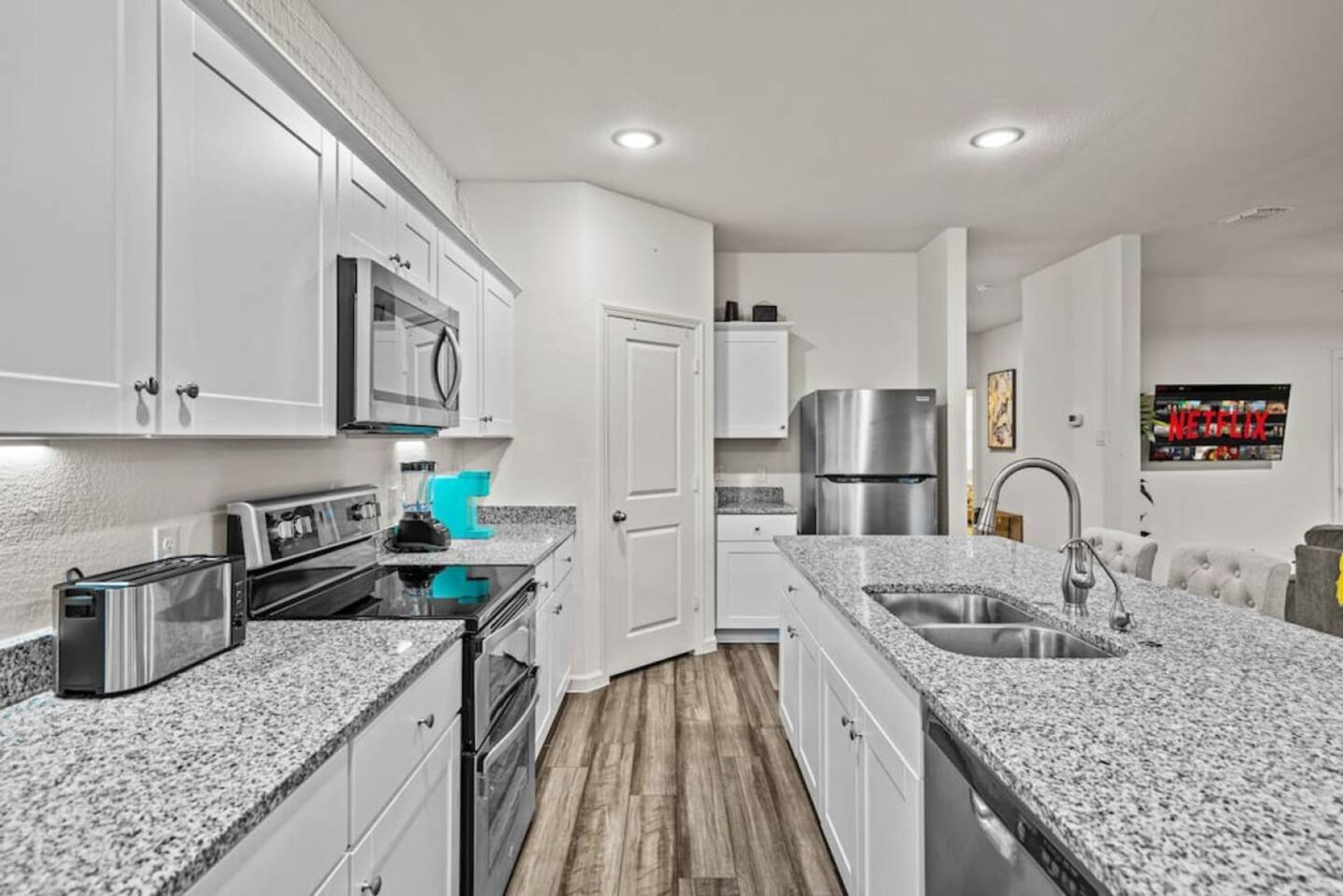 A modern kitchen with white cabinets, granite countertops, stainless steel appliances, and a built-in microwave.