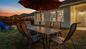 Une terrasse avec une table et des chaises en métal, un parasol rouge et un foyer.