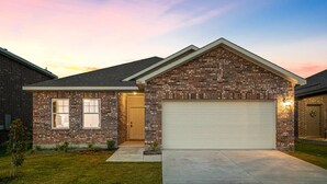 Une maison de plain-pied en briques, avec un garage, une porte d’entrée et un petit jardin à l’avant.
