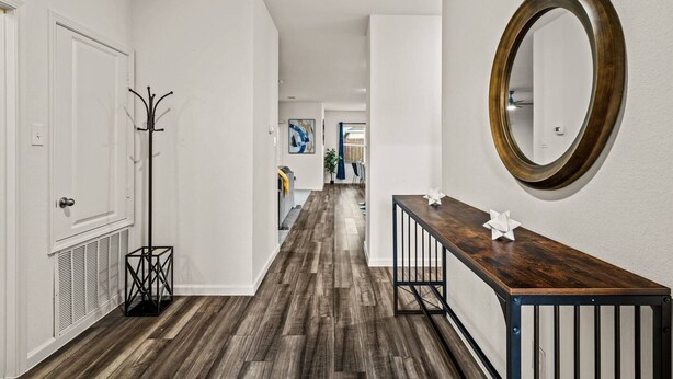 Un couloir avec un plancher en bois, des murs blancs, un porte-manteau et un miroir sur le mur de droite.
