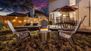 Un patio al aire libre con un brasero, dos sillas Adirondack y una mesa de comedor con sillas.