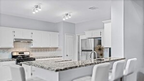 Una cocina moderna con armarios blancos, encimera de granito, electrodomésticos de acero inoxidable y taburetes para barra.