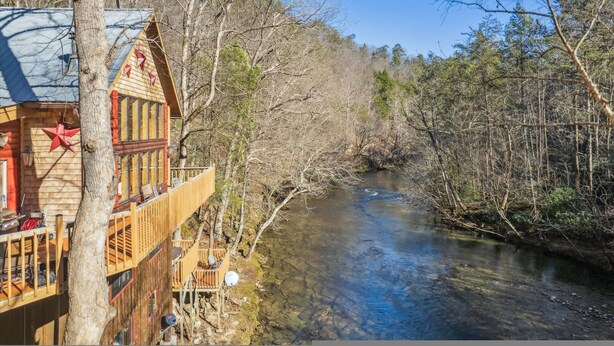 A cabin with a balcony overlooking a river, surrounded by trees.