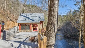 A cabin with a metal roof, a red door, and a stone foundation.