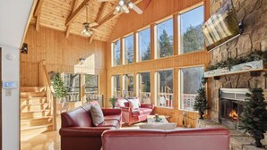A spacious living room with wooden floors, a fireplace, and large windows offering a view of the outdoors.
