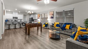 Una sala de estar moderna con una mesa de fútbol, un sofá gris con cojines azules y amarillos, y una mesa redonda de centro.