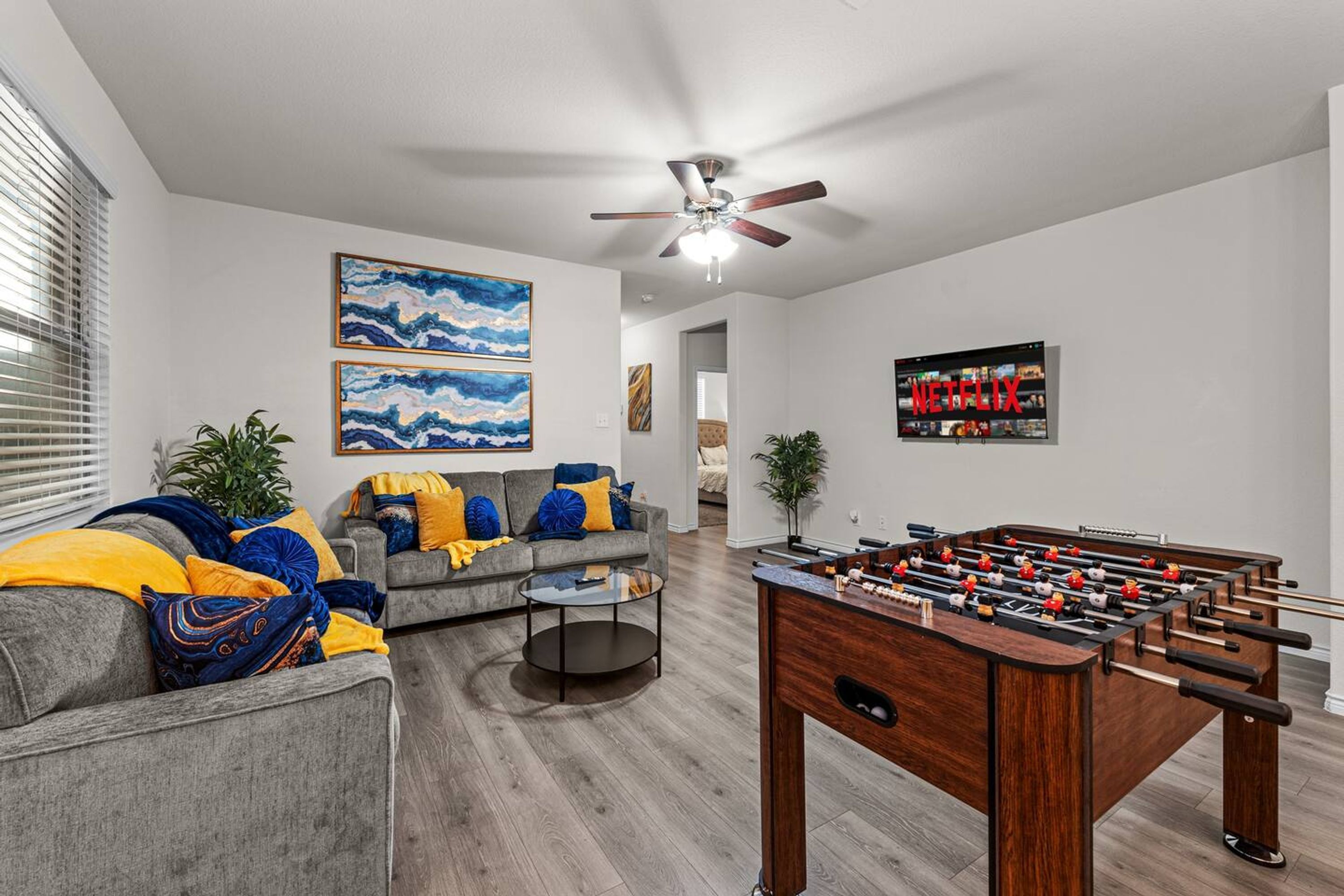 A living room with a grey sofa, colorful cushions, a foosball table, and artwork on the walls.