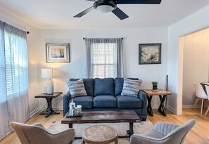 A living room with a sofa, coffee table, and chairs. There is a ceiling fan, a lamp, and two framed pictures on the wall. - Affordable 2BR Getaway Near Plaza District Lilac1 (Midwest City)