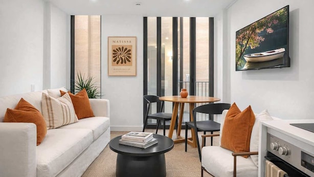 A modern living room with a sofa, coffee table, chairs, a dining table, and a kitchen area. - Perfectly Paired | Dual 1BRs + Pool & Gym | CBD (Wellington City)