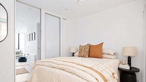 A bedroom with a bed, bedside tables, a lamp, and a view into another room. - Perfectly Paired | Dual 1BRs + Pool & Gym | CBD (Wellington City)