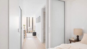 A modern bedroom with a large bed, a bedside table with a lamp, and a view of a balcony with a chair and a plant. - Perfectly Paired | Dual 1BRs + Pool & Gym | CBD (Wellington City)