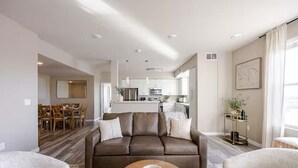 A modern living room with a brown leather sofa, a round coffee table, and a dining area in the background. - Amazing Water View w Jacuzzi Sky Lounge (Sparks)