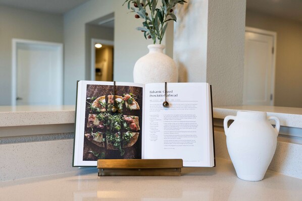 A framed recipe book on a stand, a white vase with greenery, and a kitchen counter. - Amazing Water View w Jacuzzi Sky Lounge (Sparks)