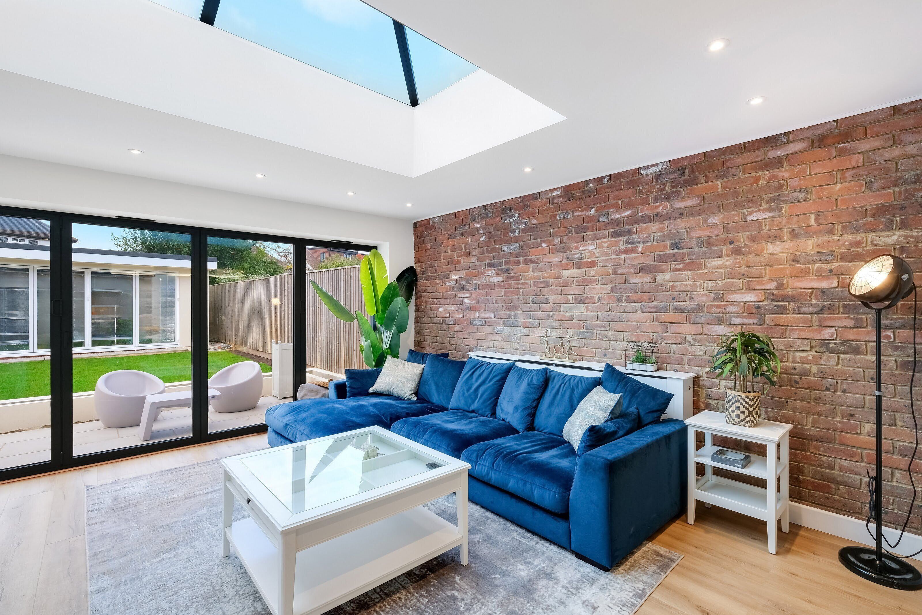 A modern living room with a blue sofa, a glass coffee table, and a brick wall.