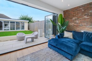 A modern living room with a blue sofa, a white coffee table, and a large potted plant. - Sustainable Stays (Bushey)