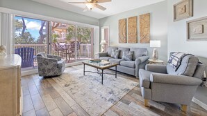 A spacious living room with a large sliding glass door leading to a balcony, a ceiling fan, a grey sofa set, and a coffee table. - Wonderfully Updated Two Bedroom Condominium! (Hilton Head Island)