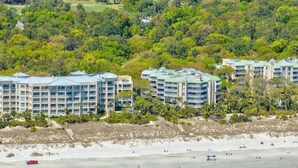 A beachfront hotel with multiple buildings, a sandy beach, and a forested area in the background. - Wonderfully Updated Two Bedroom Condominium! (Hilton Head Island)