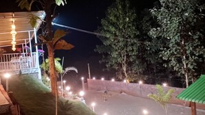 A nighttime view of a courtyard with a paved area, a small pool, and a covered seating area with string lights. - HIYAS RETREAT (Sonapur)