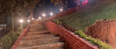 A nighttime staircase with brick walls and greenery on the sides, illuminated by street lamps.