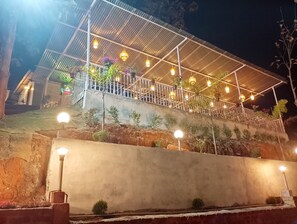 A building with a covered outdoor area, railings, and multiple light fixtures. - HIYAS RETREAT (Sonapur)