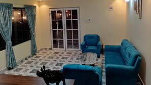 A living room with a blue sofa, a blue armchair, a marble coffee table, and a black dog statue. - HIYAS RETREAT (Sonapur)