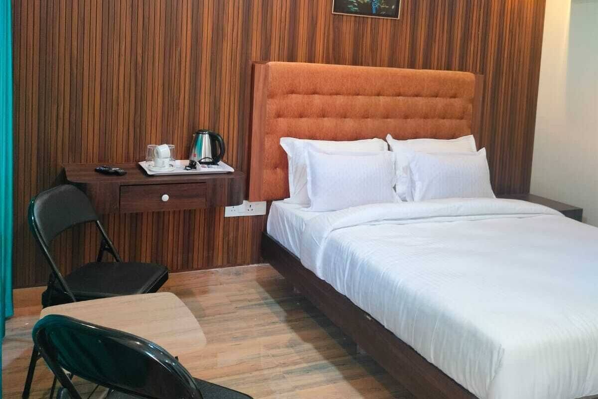 Habitación de hotel con pared de paneles de madera, una cama grande con ropa de cama blanca, un escritorio con silla y una mesita con hervidor y taza.