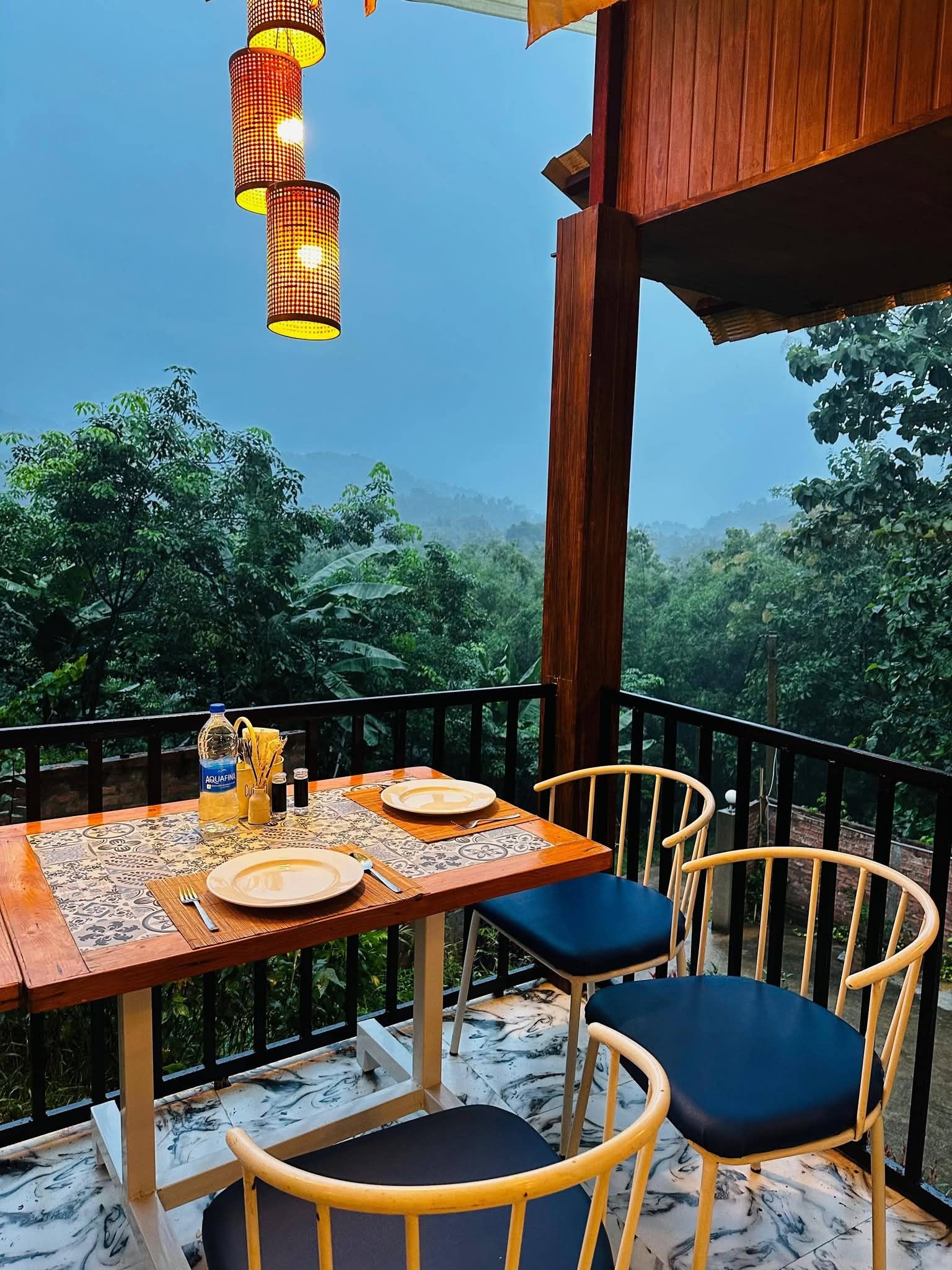 An outdoor dining area with a table set for two, surrounded by chairs, and a view of a forested landscape.
