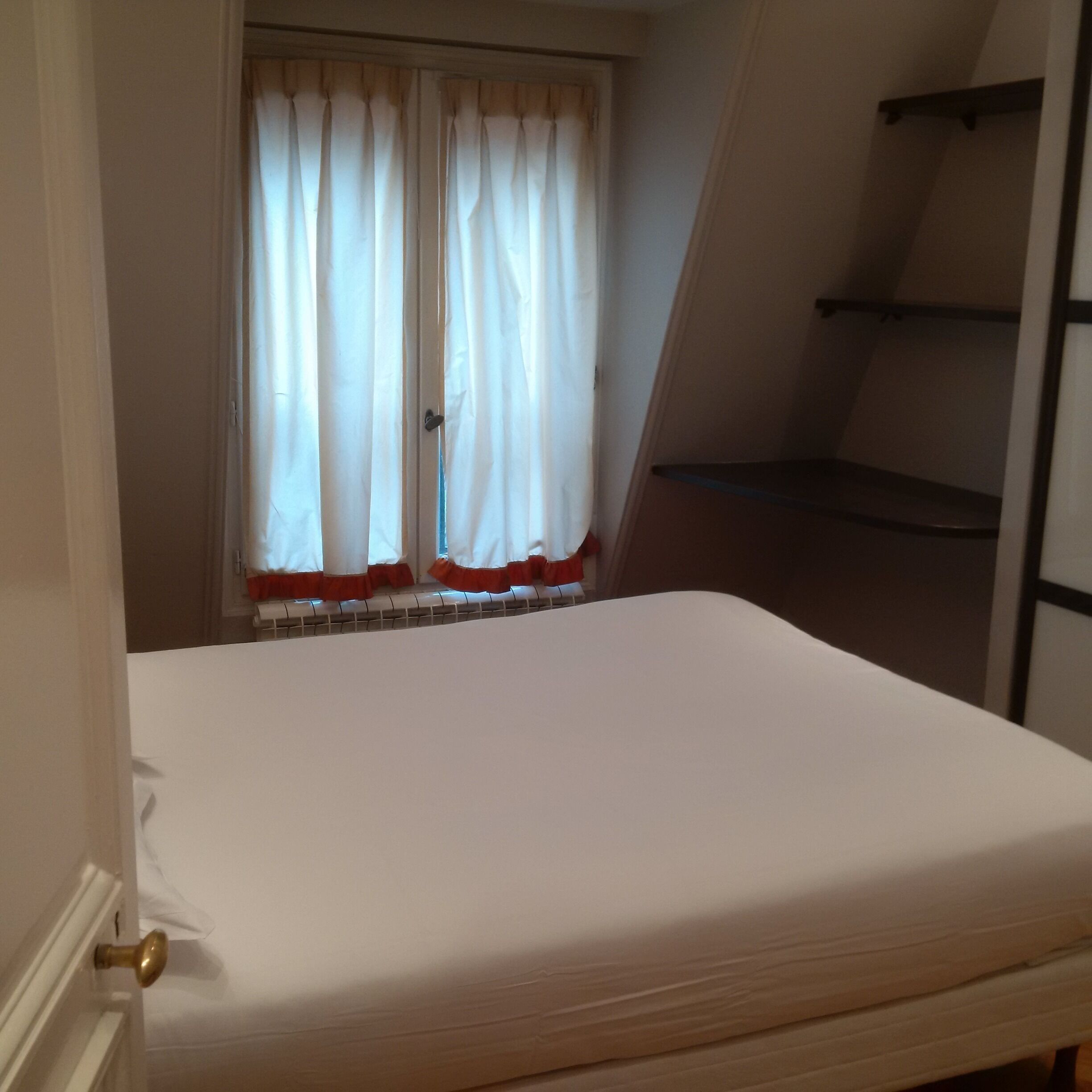 Een slaapkamer met een enkel bed, een raam met gordijnen en een schuine balkenkap.