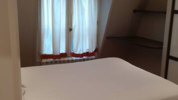 Een slaapkamer met een enkel bed, een raam met gordijnen en een schuine balkenkap.