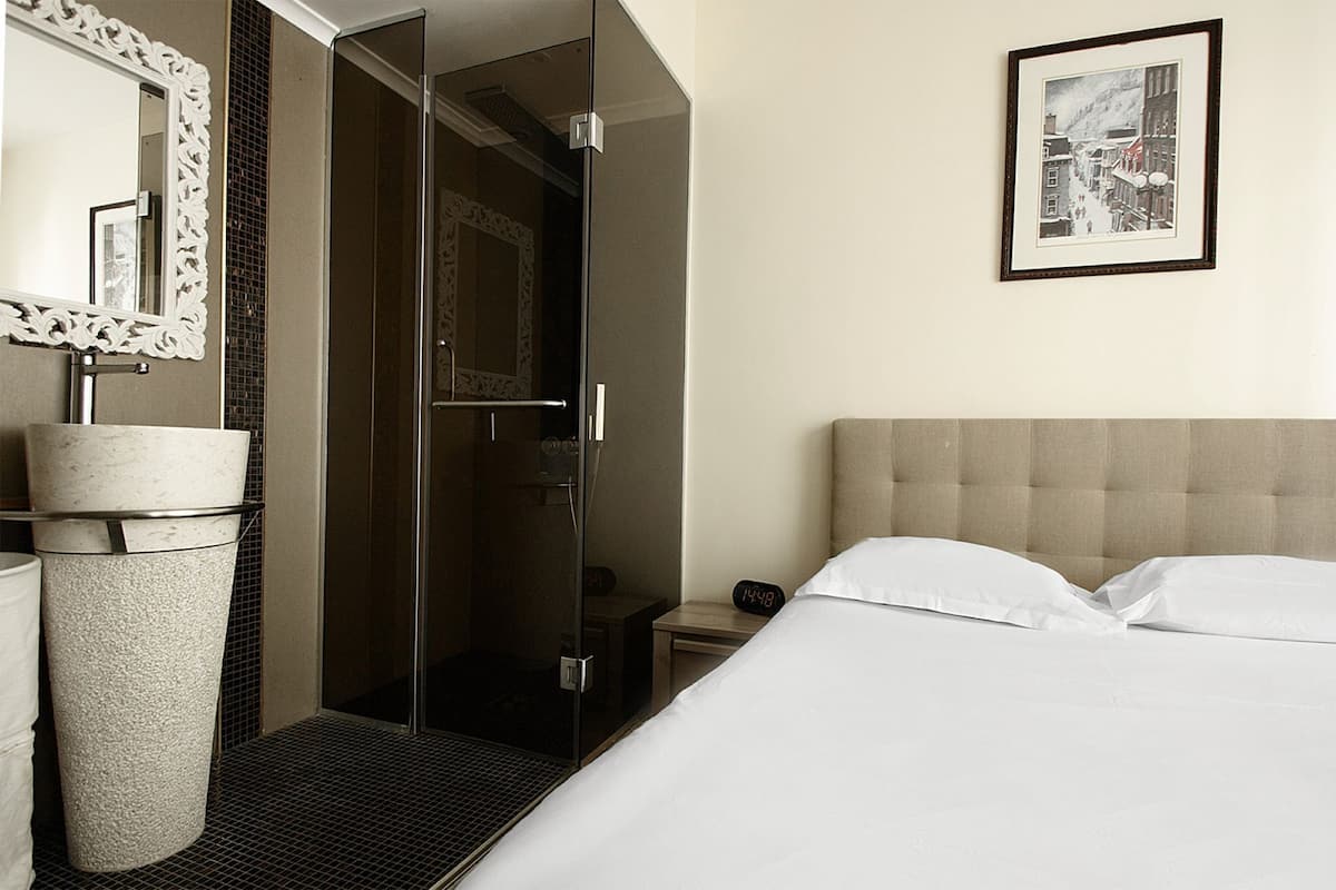 Ein Hotelzimmer mit Bett, einem Badezimmer mit Dusche, Waschbecken und einem gerahmten Bild an der Wand.