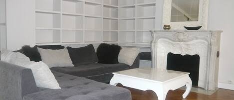 Una sala de estar con sofá gris, una mesa de centro blanca y una chimenea blanca con un espejo arriba.