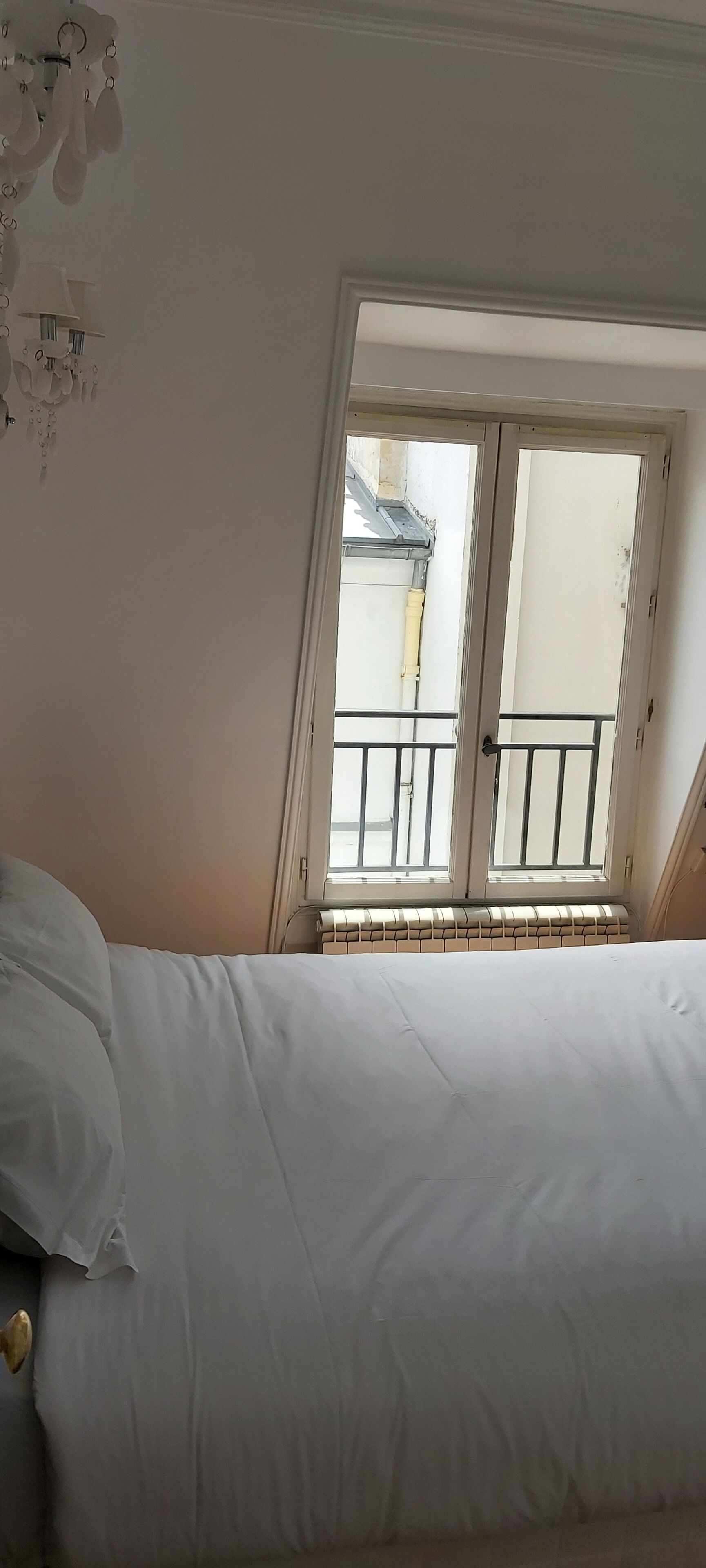 A bedroom with a bed, a window with a view of the outside, and a radiator under the window.
