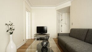 Un soggiorno moderno con un tavolino in vetro, un divano grigio, un vaso bianco con fiori e un televisore a schermo piatto su un supporto.
