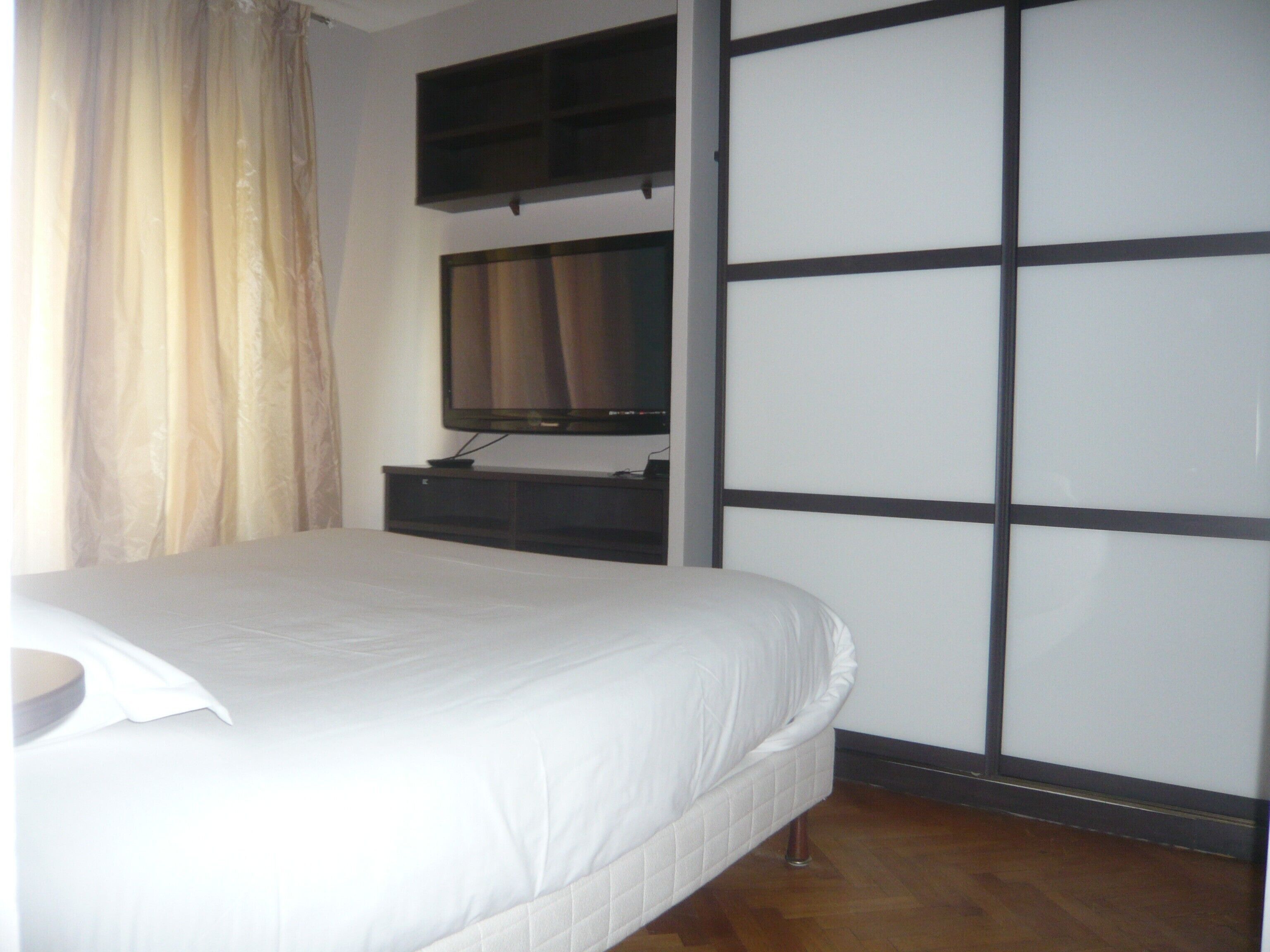 A bedroom with a bed, a television mounted on the wall, and a sliding door.