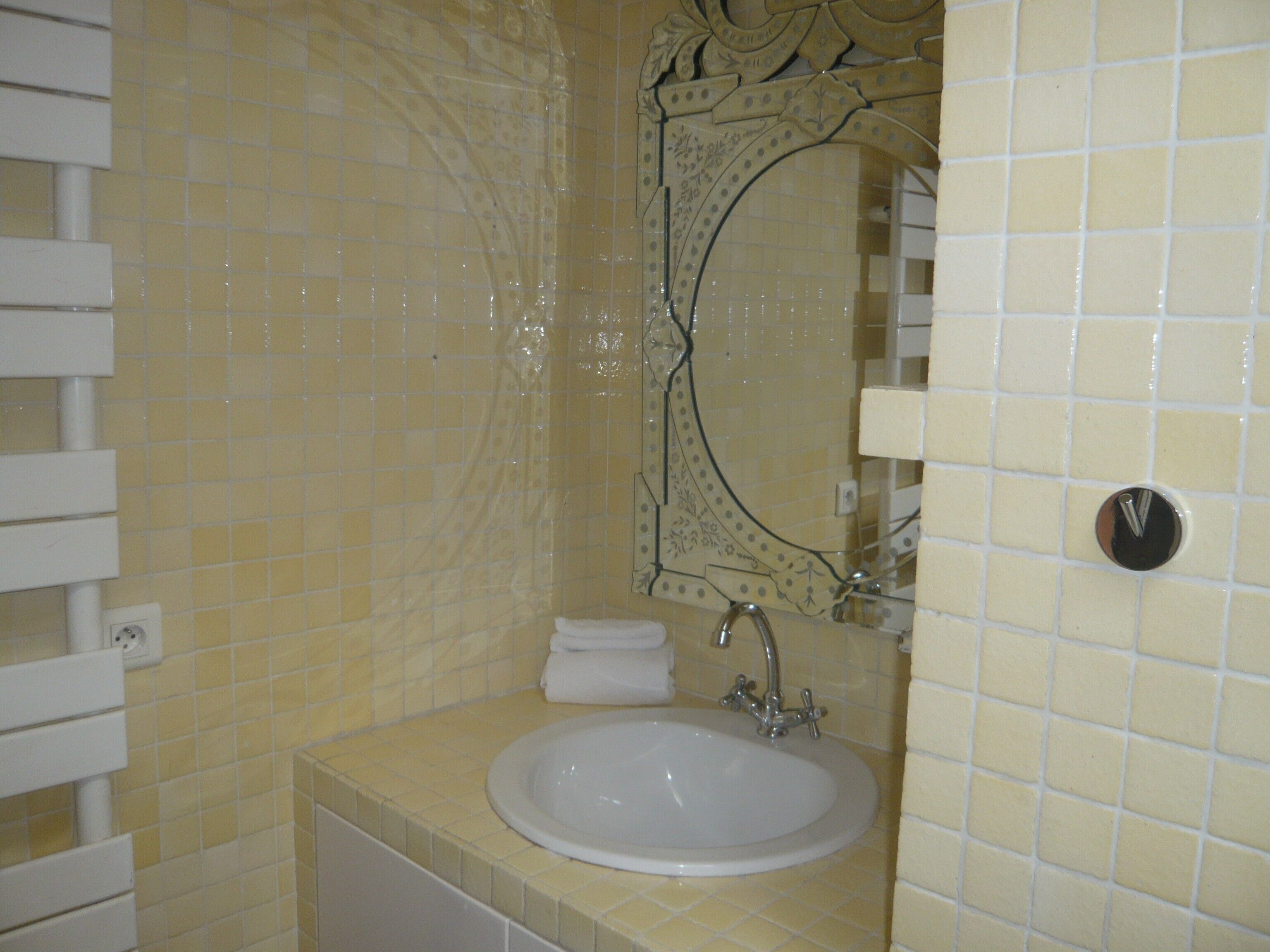 Een badkamer met een witte wastafel, een spiegel met decoratieve details en een handdoekrek.