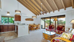 A spacious living area with a wooden ceiling, a dining set, and a view through large sliding doors to an outdoor deck. - Maui Kamaole K-207 Recently Remodeled, Views, Pools, Hot Tub, A/C, W/D (Kihei)
